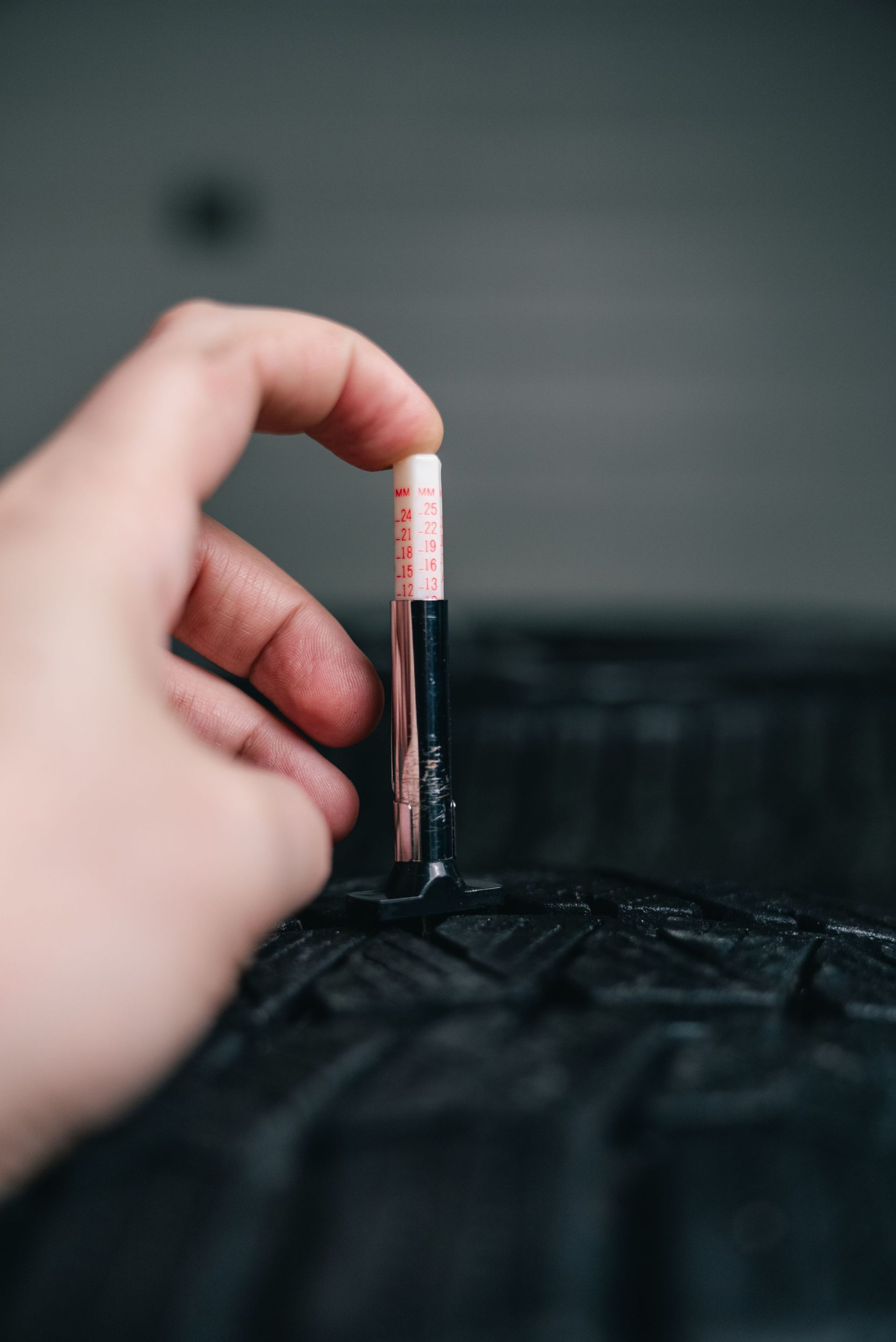 Close-up of hand using a tread depth gauge on a tire. Safety and maintenance check.