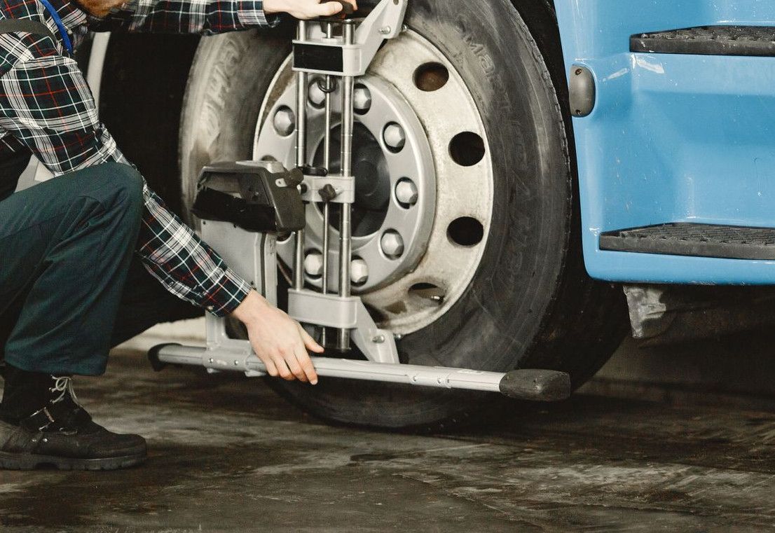 Mechanic performing tire alignment on a truck in an indoor workshop setting.
